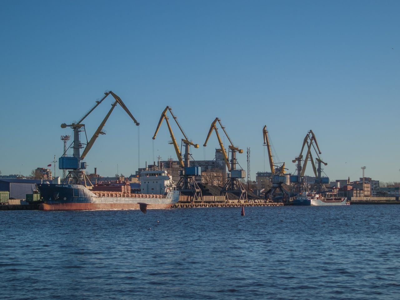 Image of an industrial shipyard with cranes and ships on a sunny day.