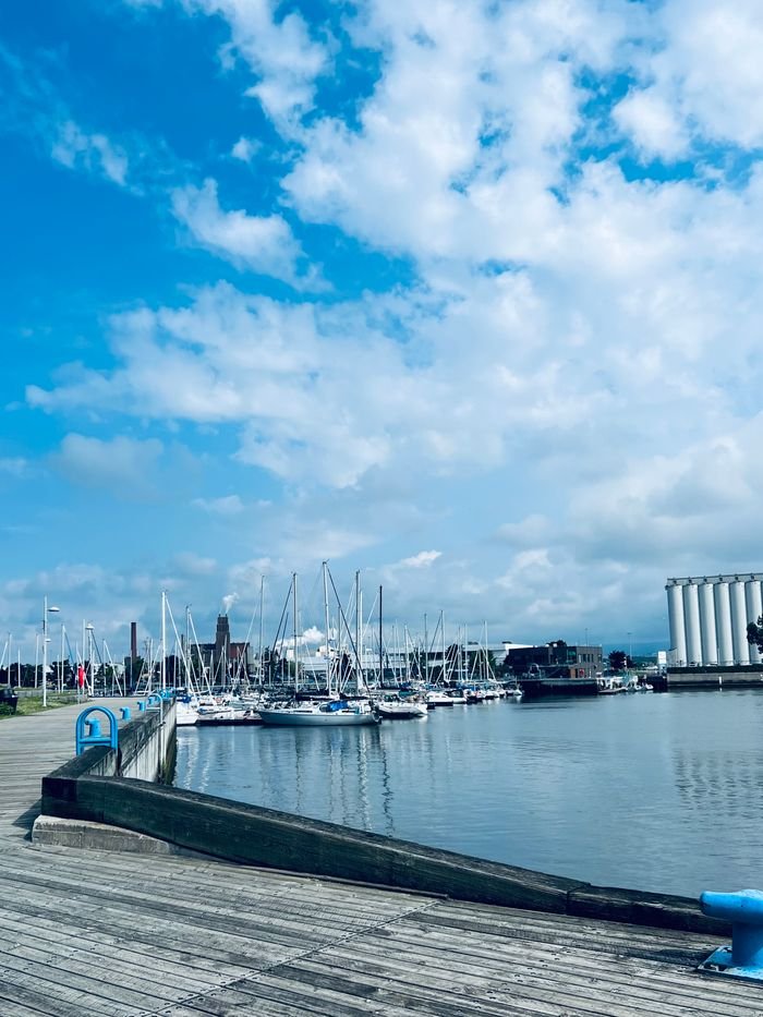A serene marina with yachts moored under a vibrant blue sky and fluffy clouds.